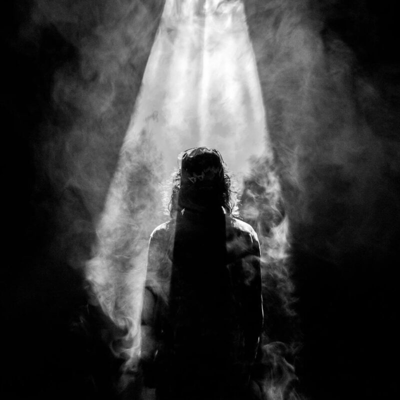 photograph of person facing opposite in smoky spotlight